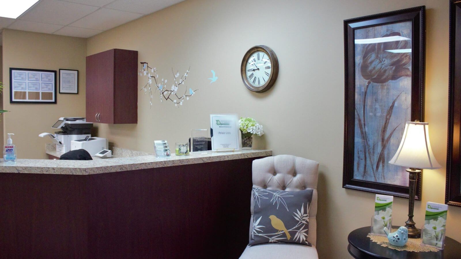 Reception area with curved burgundy desk, wall clock, lamp, framed art, and upholstered chair