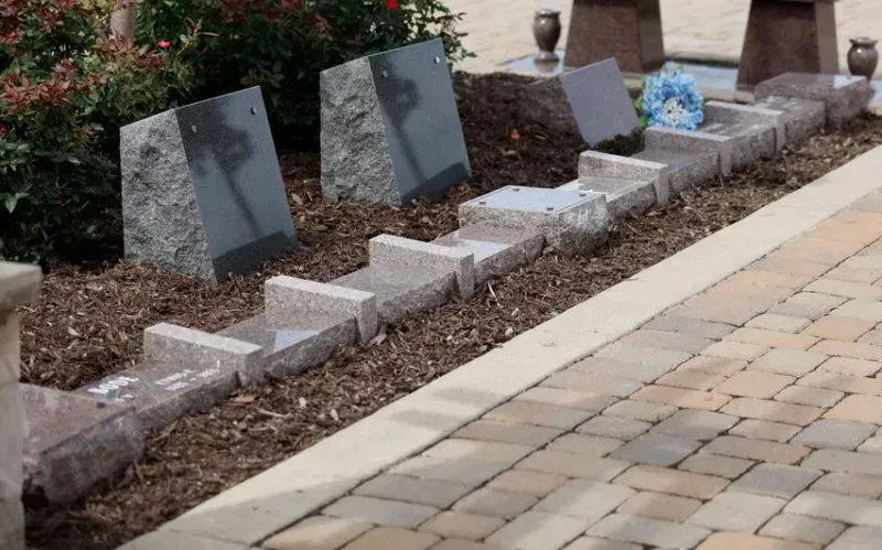 Garden memorial with upright gray plaques and small stone markers beside a paved walkway