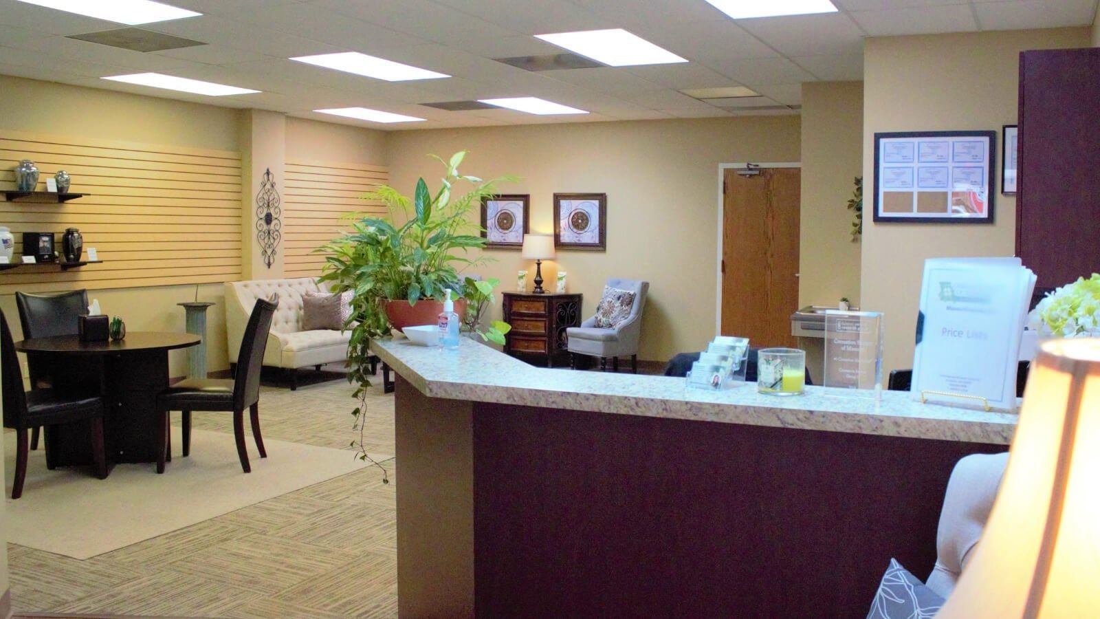 Reception area with curved desk, chairs, potted plants, and framed wall art in an office lobby