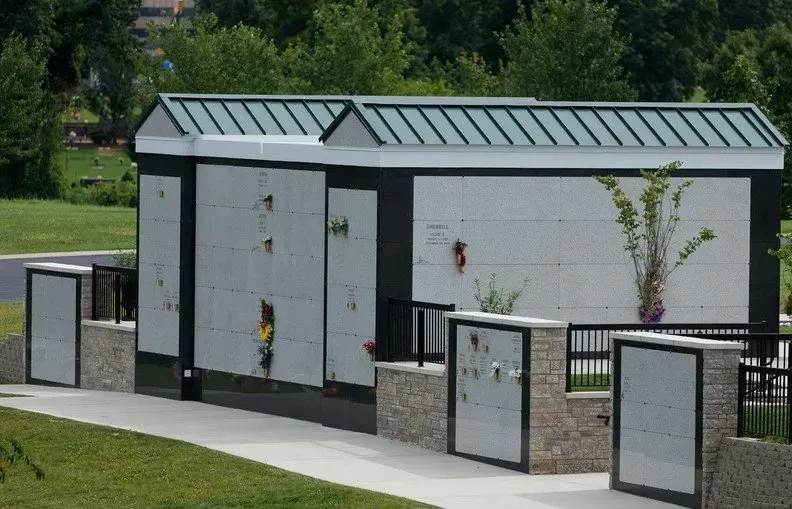 Modern restroom building with gray doors and green metal roof behind a low fence