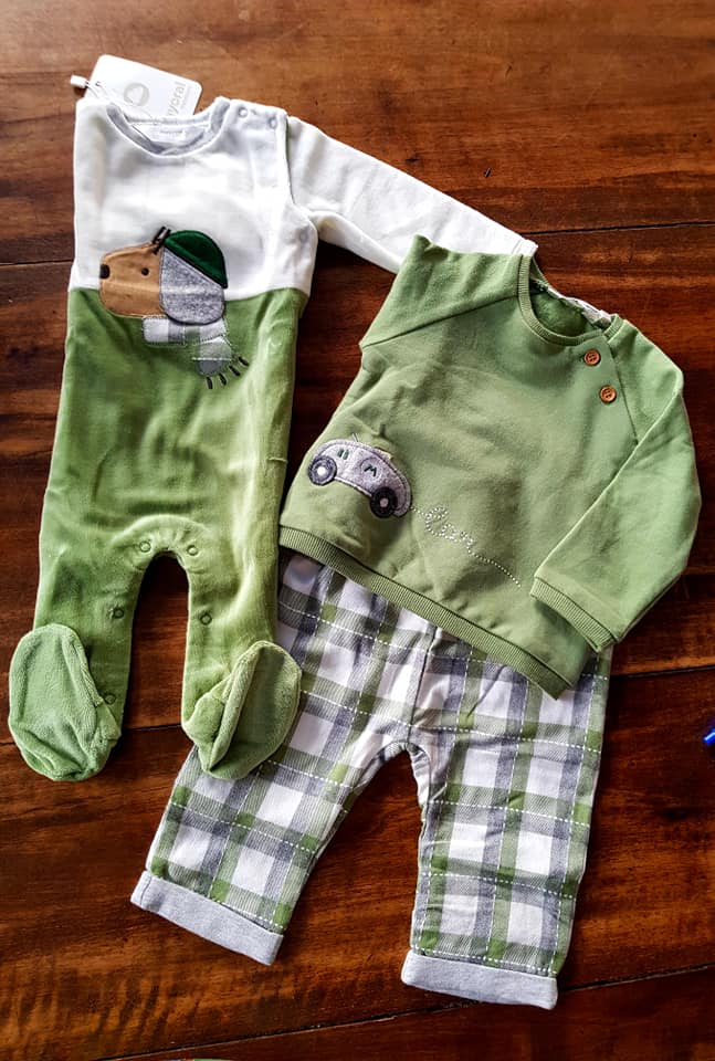 Un vestito verde e bianco da neonato è appoggiato su un tavolo di legno.