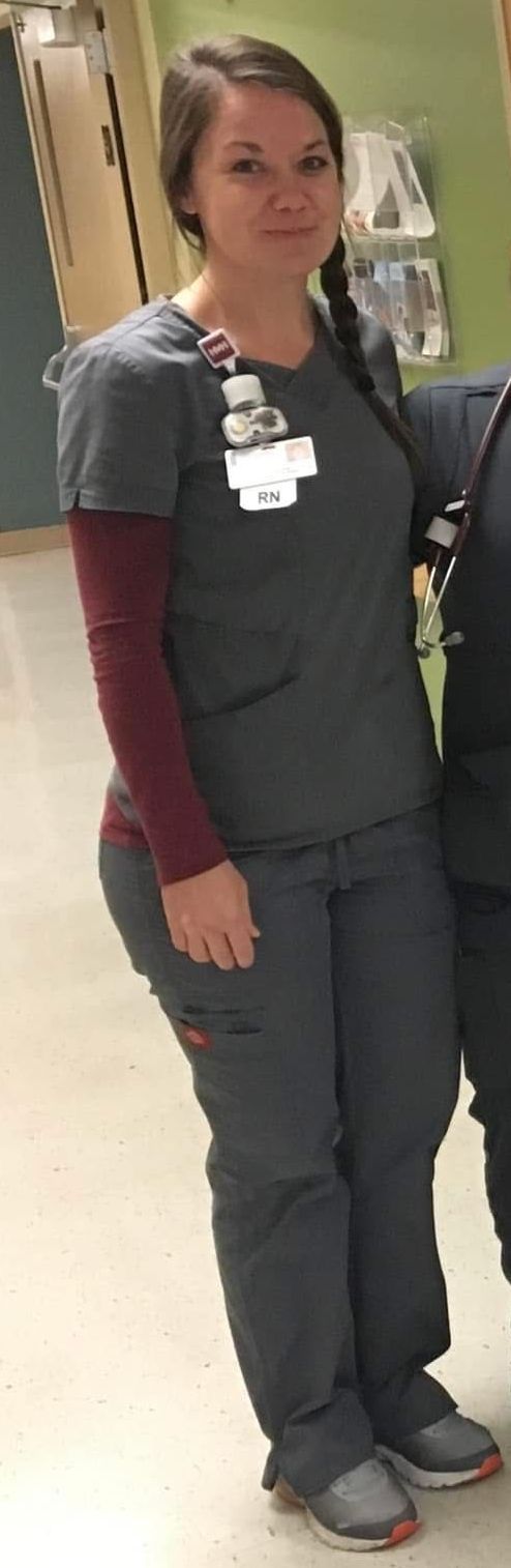 A woman in scrubs is standing in a hospital hallway.