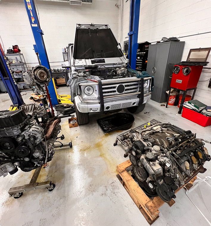 A white SUV under repair in a garage with two engines on stands in the foreground. | Kensington Motor Cars