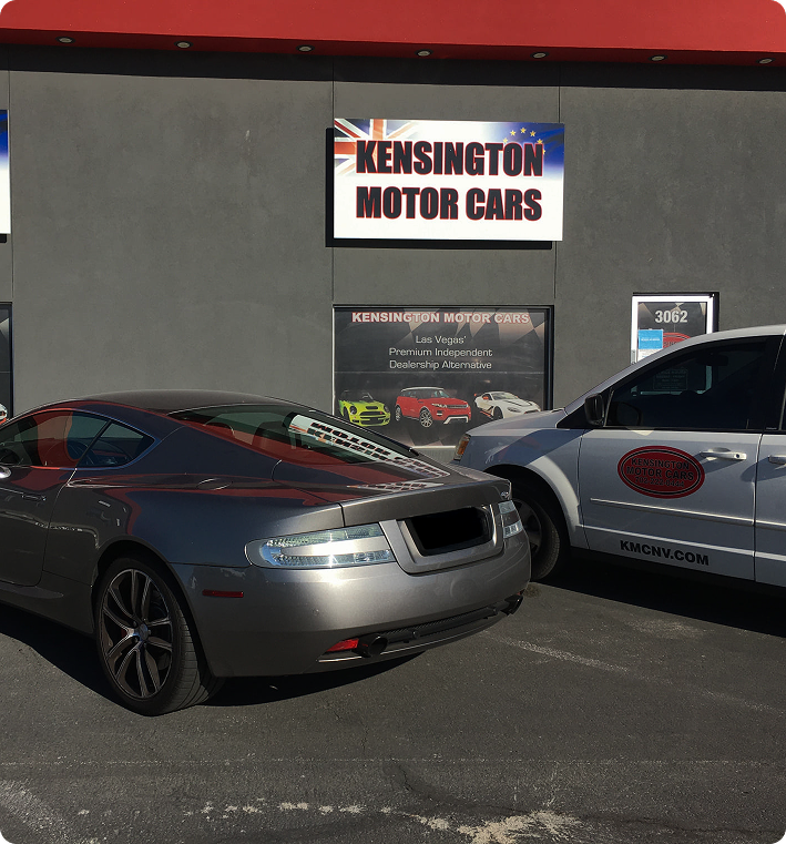 Grey Aston Martin sports car parked outside Kensington Motor Cars dealership.