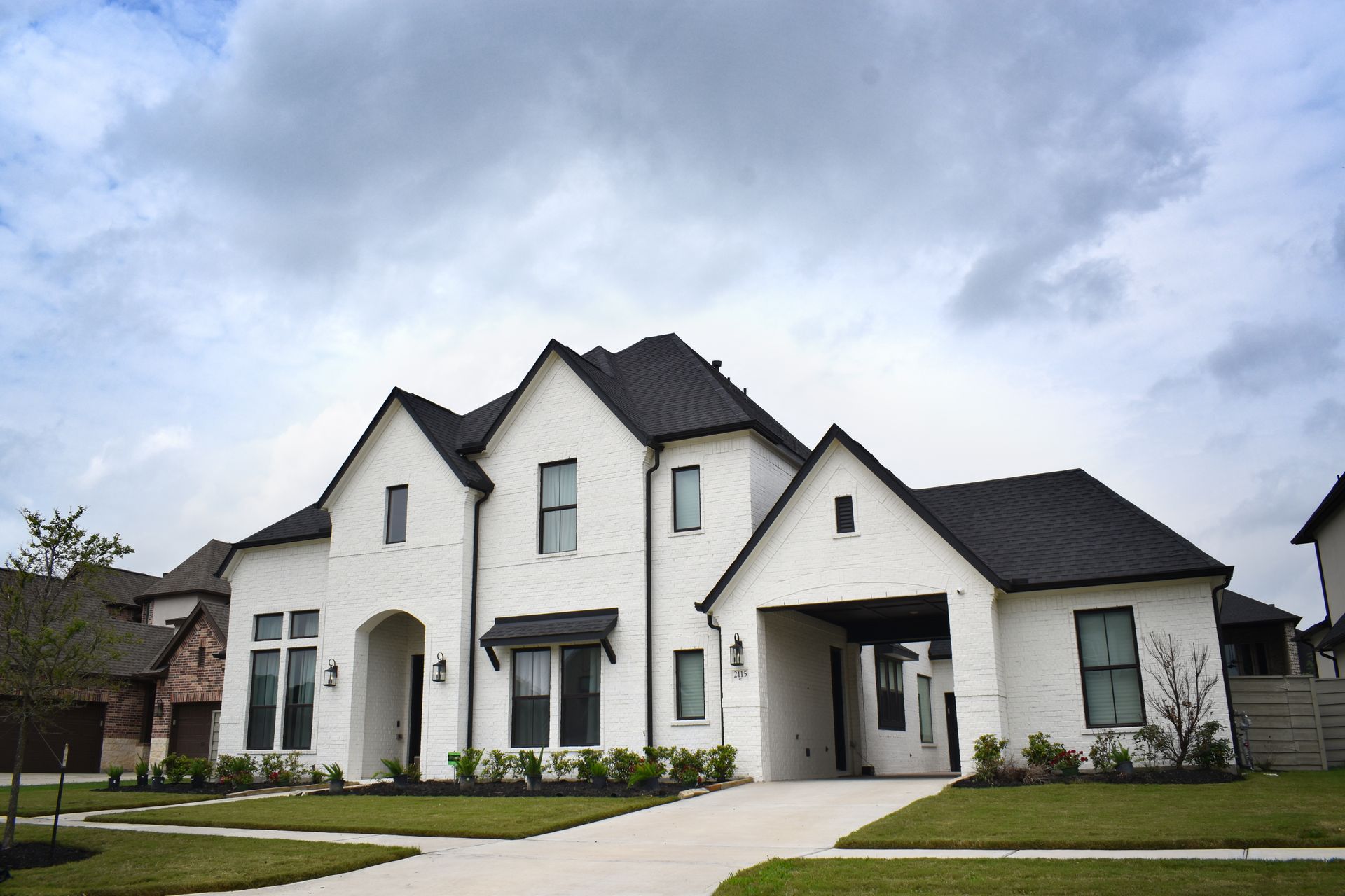 A large white house with a black roof is sitting on top of a lush green lawn.