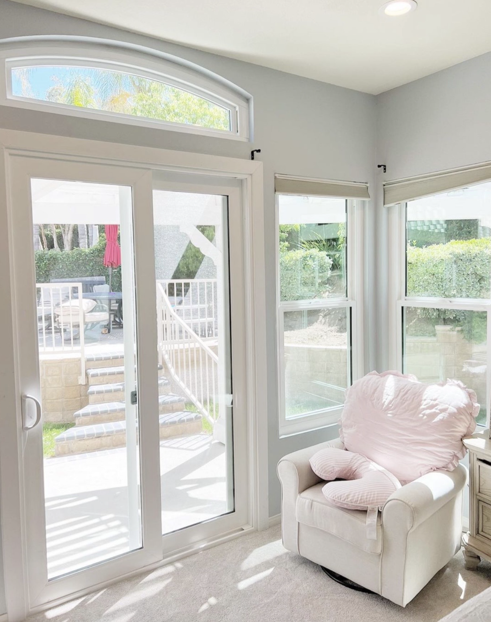 A light-filled room with a patio door, chair with pink pillow, and three windows.
