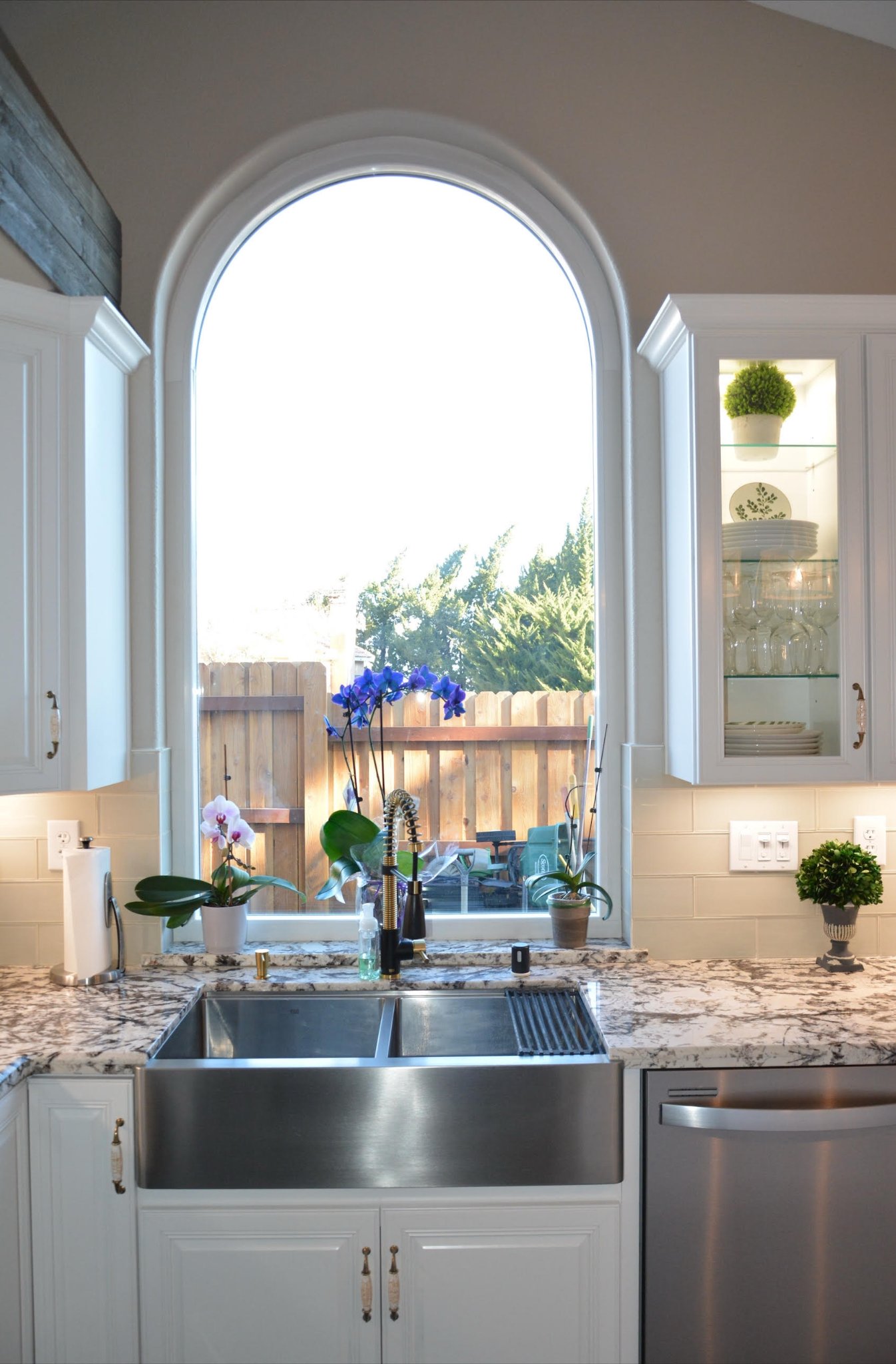 Kitchen with large arched window above stainless steel sink, white cabinets, and granite countertop.