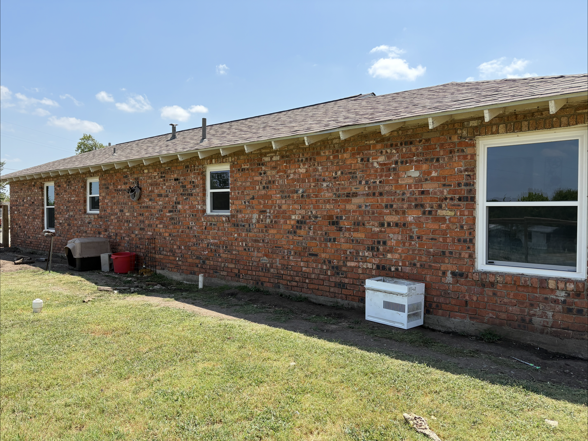 Red brick house exterior with several windows, grass, and a blue sky.
