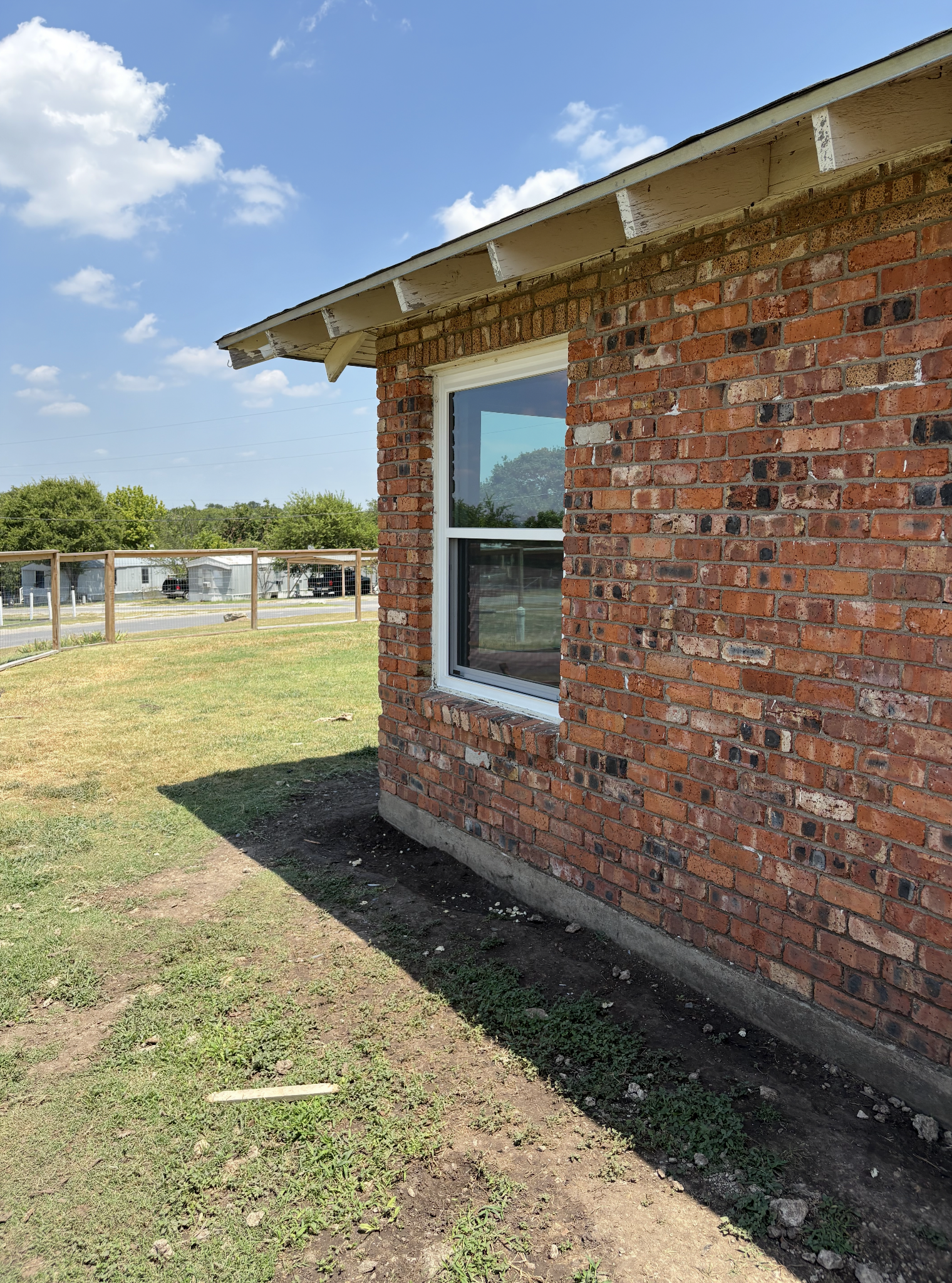 Brick building corner with a window on a sunny day. Green grass and blue sky are visible.