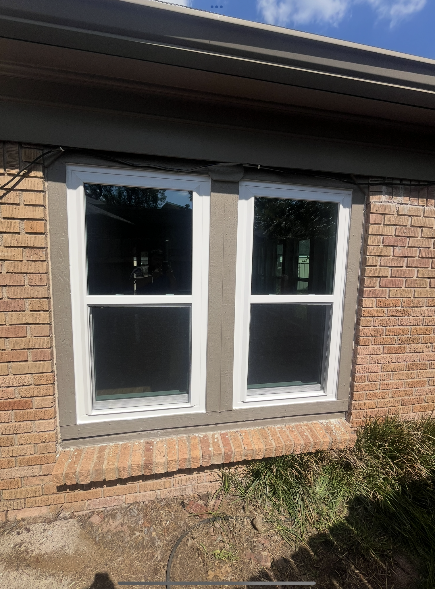 Two rectangular windows with white frames set in a brick wall, with gray trim.