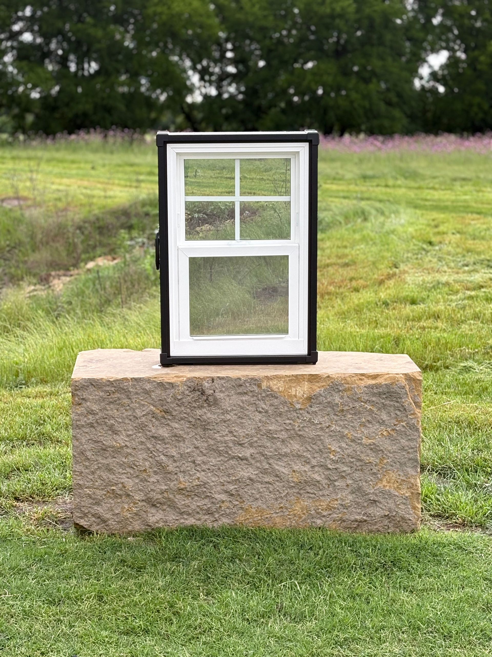 Window in black frame on a stone block in a grassy field.