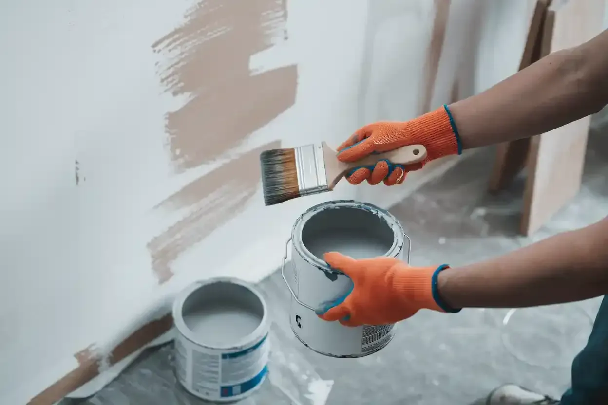 A person is painting a wall with a brush and two cans of paint.