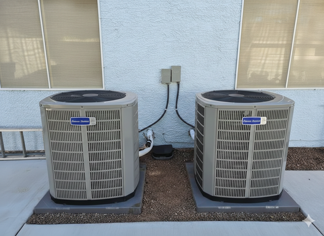 Two air conditioning units on concrete pads against a stucco wall, with electrical boxes above.