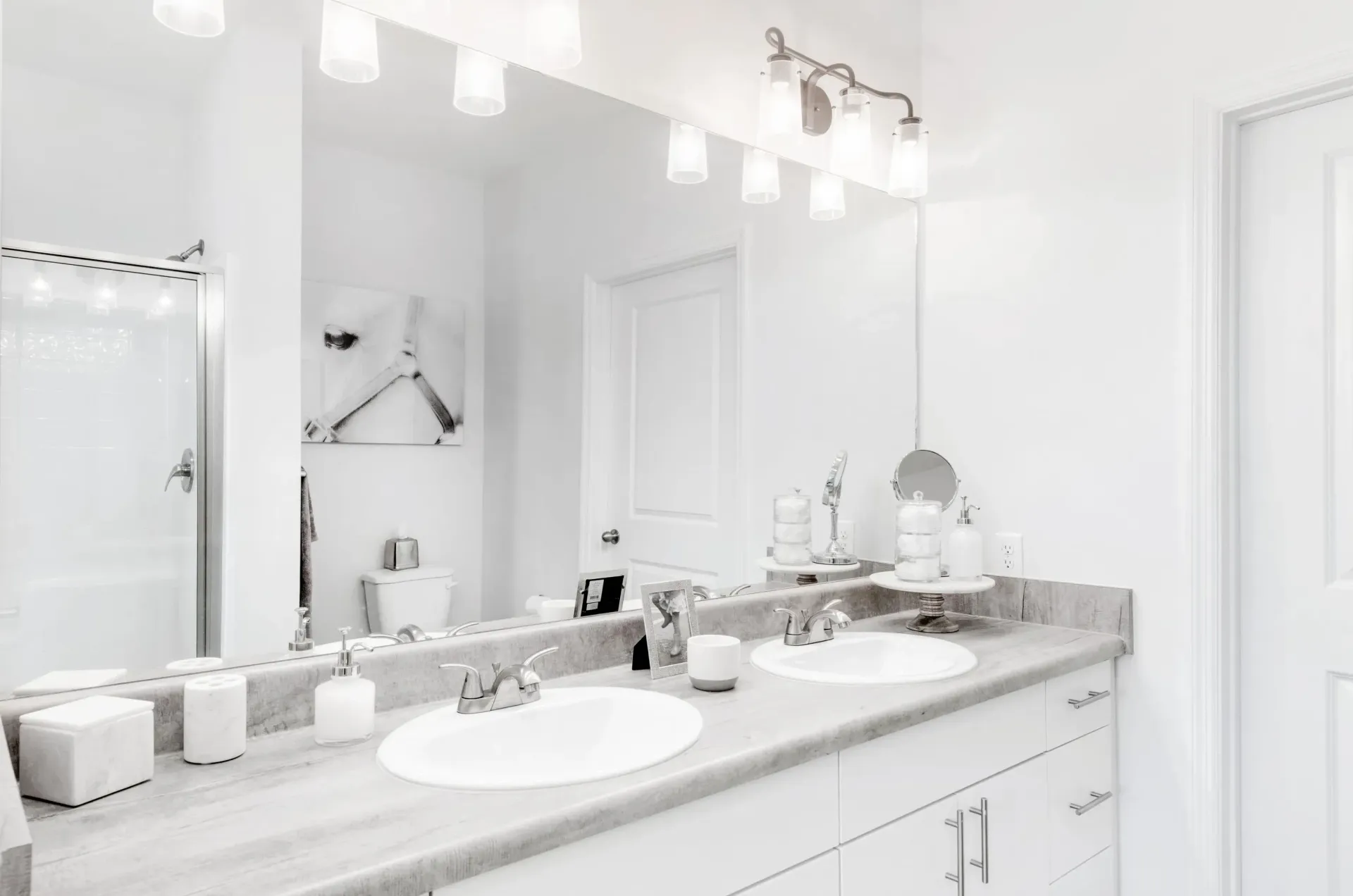 White bathroom with double vanity, large mirror and glass shower.