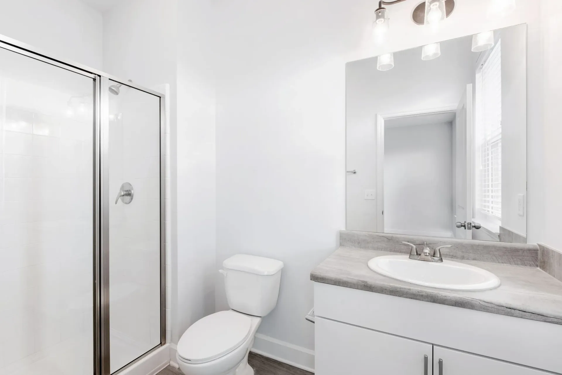 Bright white bathroom with shower enclosure, toilet, and vanity sink.