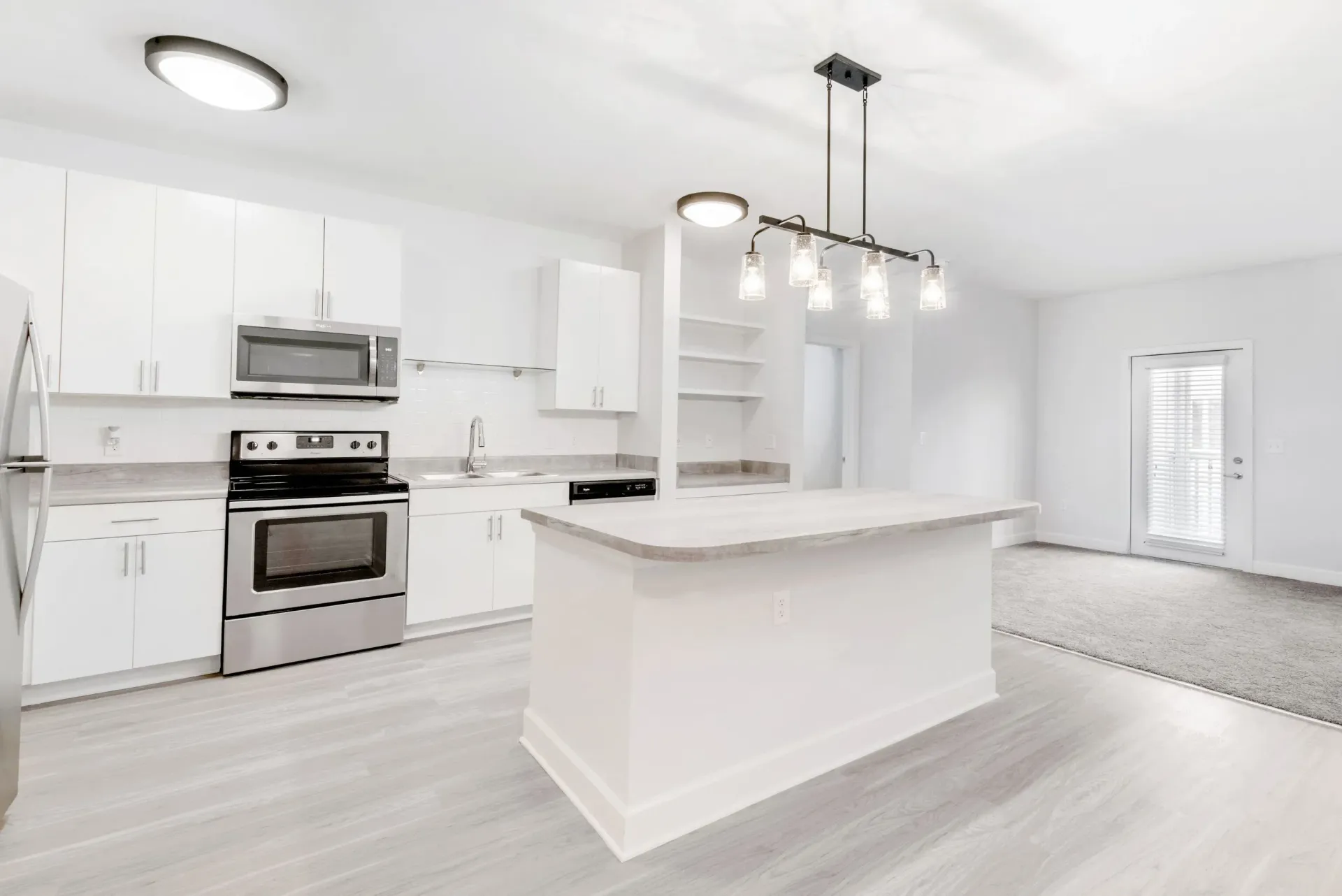Open-concept kitchen with white cabinets, island, and stainless steel appliances.