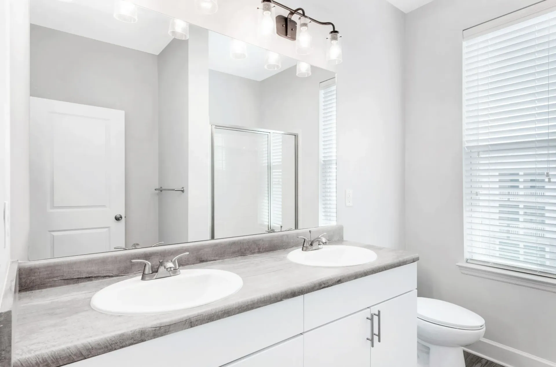 Bright bathroom with a double-sink vanity, large mirror, and a window with blinds.