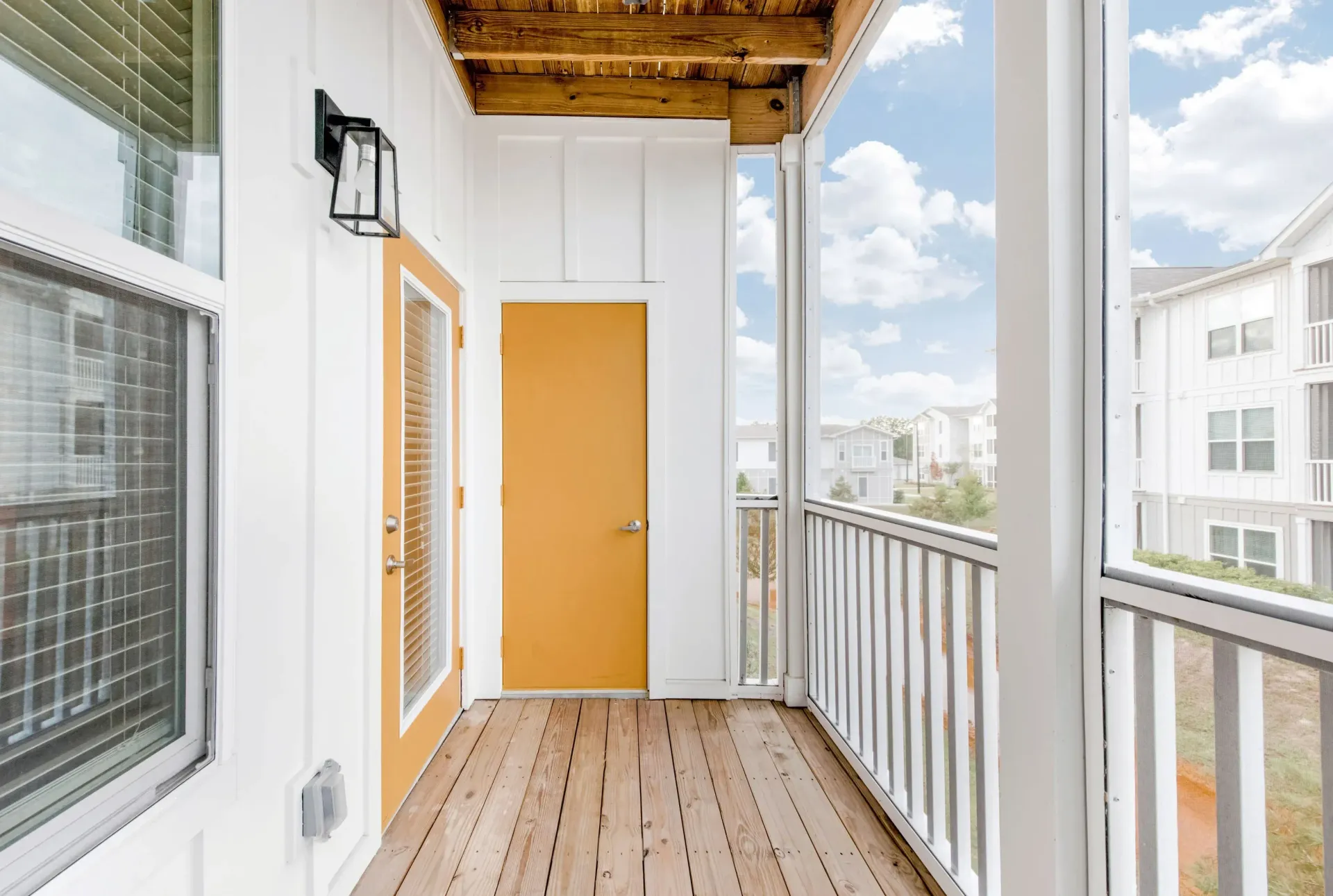 Outdoor balcony with wood deck, white walls, orange door, and railing.