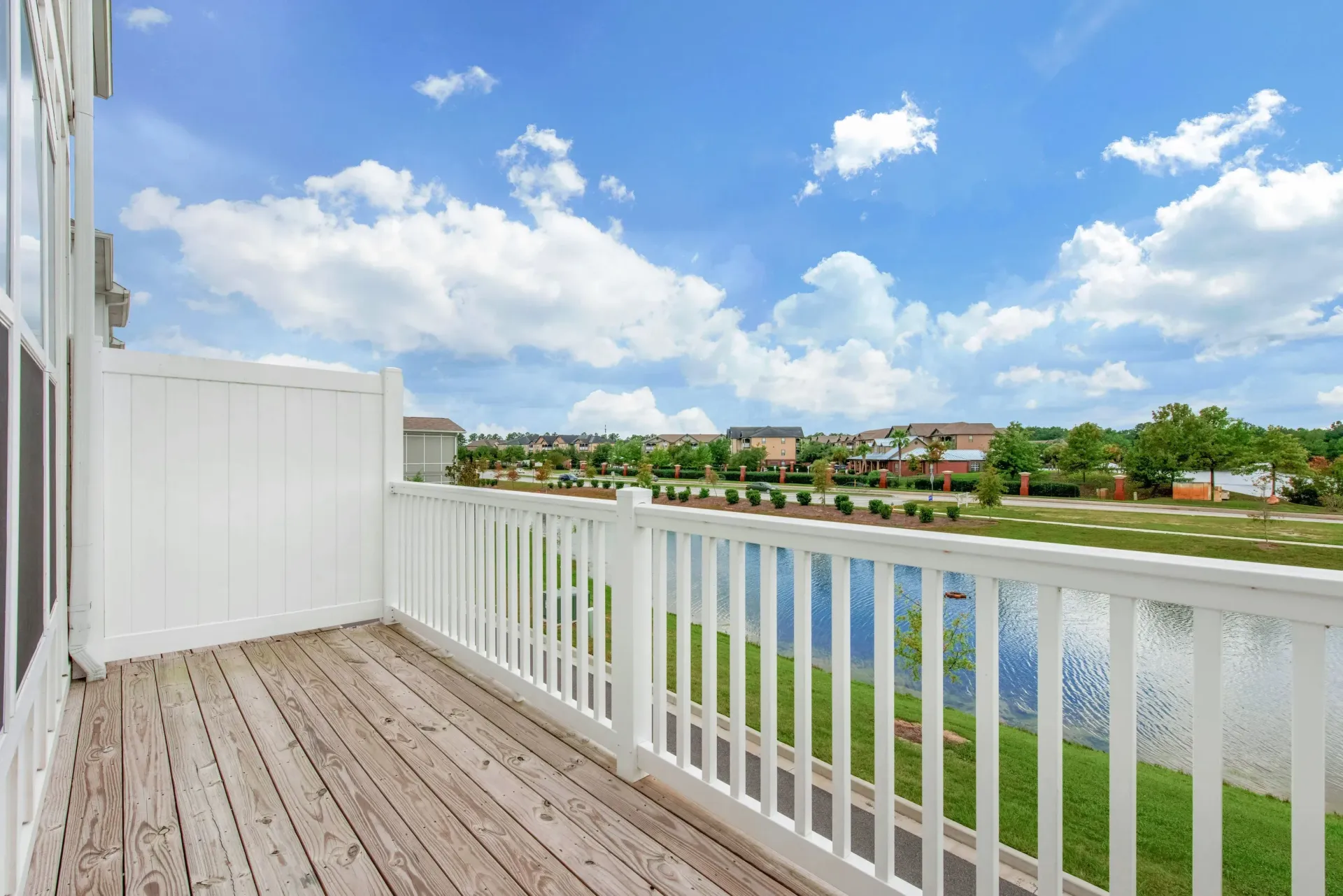 View from a balcony with white railing and wooden deck, overlooking a pond and landscaped community.