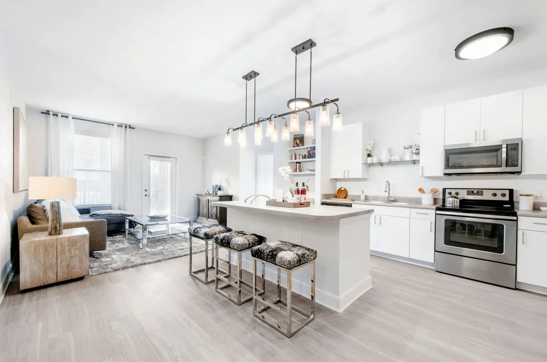 Open-concept kitchen and living area in a modern apartment with white cabinets and stainless-steel appliances.
