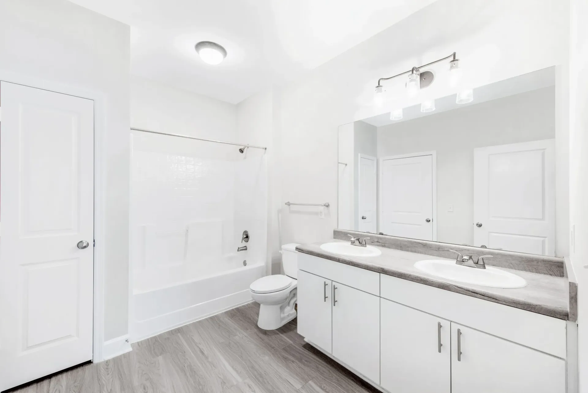 Bright bathroom with double-sink vanity, toilet, and bathtub.