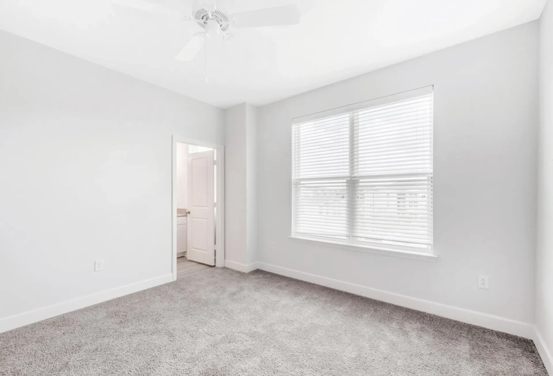 Bright empty bedroom with a window, blinds, carpet, and a ceiling fan.