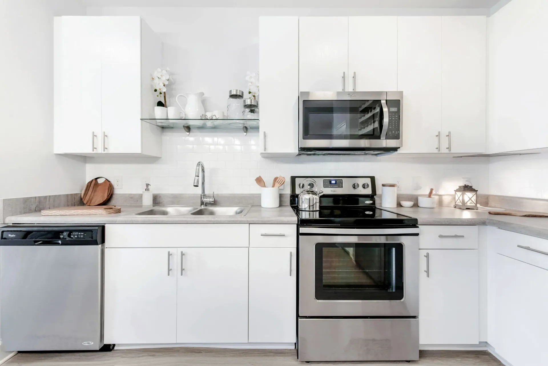 Modern white kitchen with stainless steel stove, microwave, dishwasher and double sink.