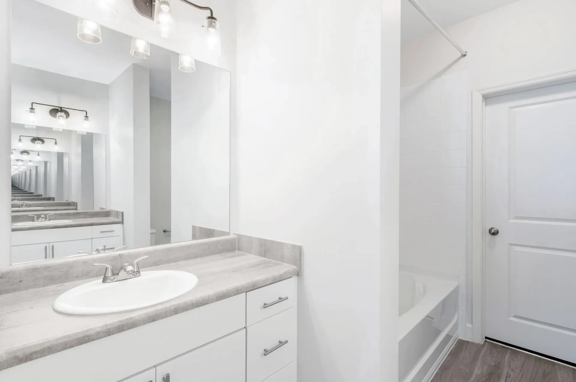Bright white bathroom with a sink, grey countertop, a large mirror, and a tub/shower.
