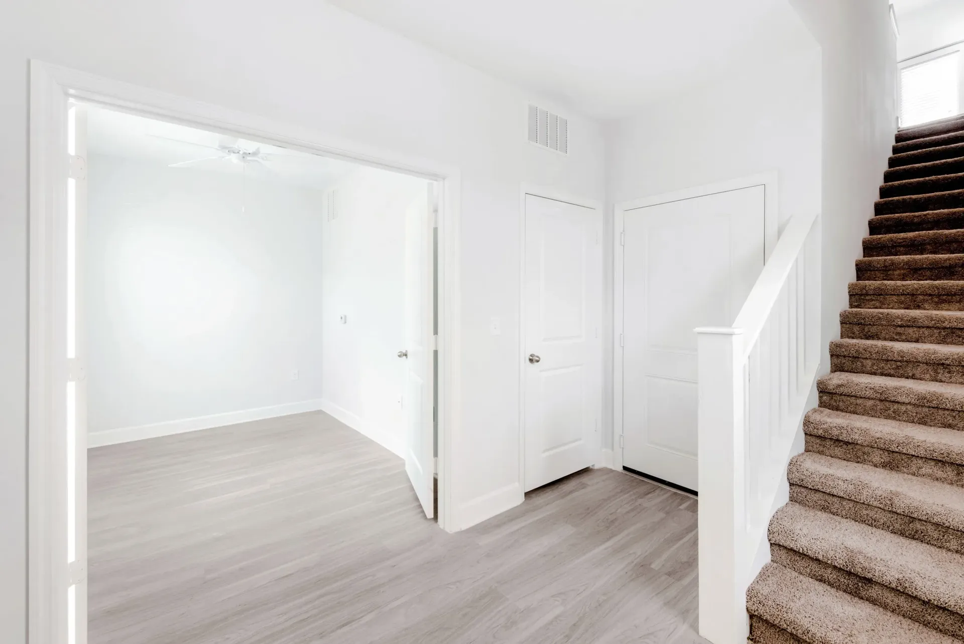 Bright white hallway with doors, light gray flooring, and a carpeted staircase.