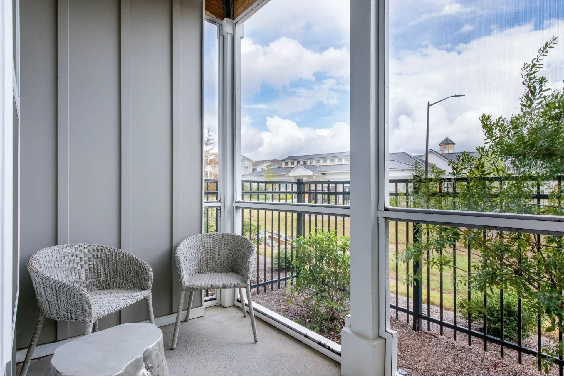 Balcony with two wicker chairs and a small table overlooking a fenced courtyard.