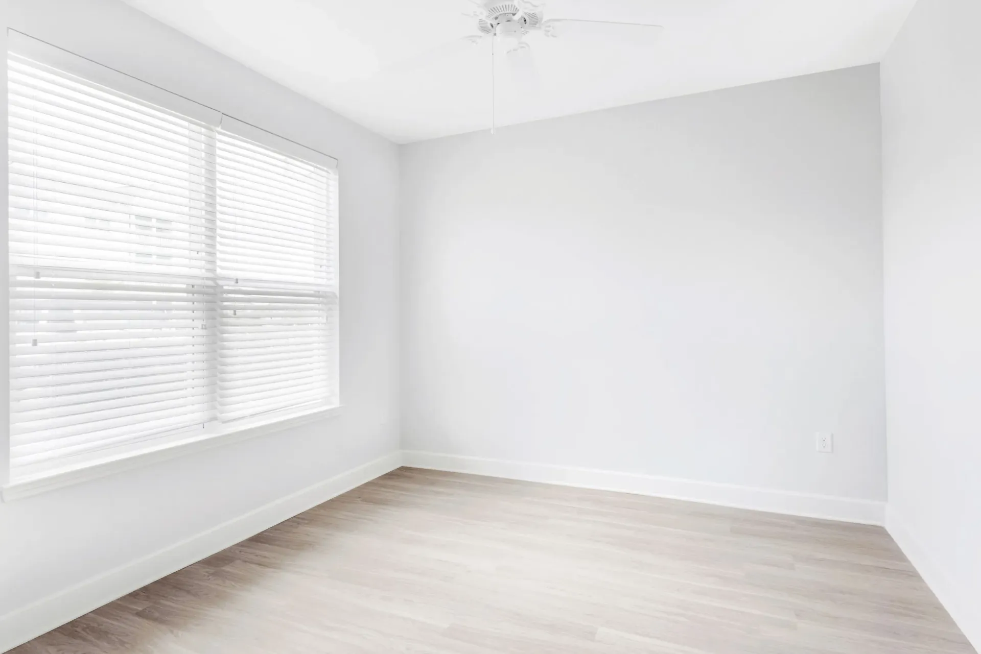Empty bedroom with light gray walls, white blinds, and a ceiling fan.