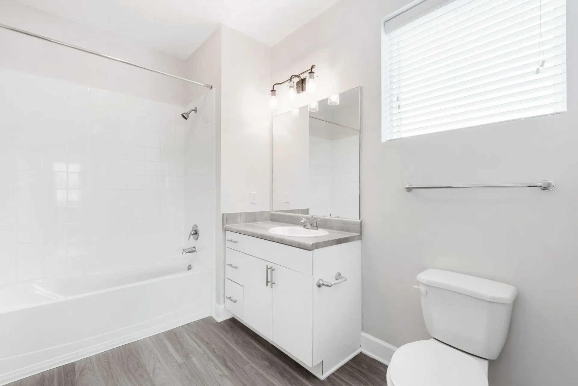 Bright apartment bathroom with white vanity, mirror, tub/shower, and toilet.