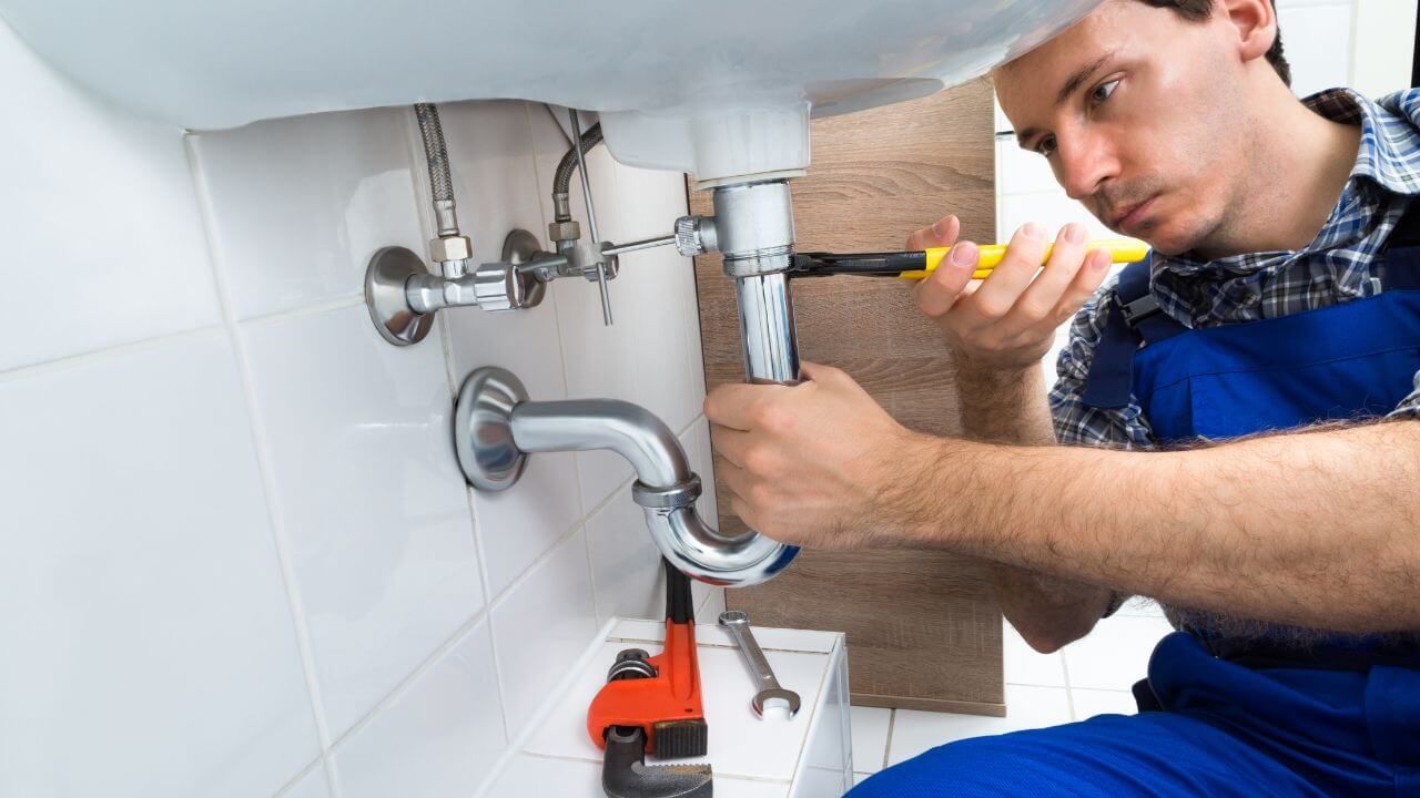 A plumber in overalls working on a sink.