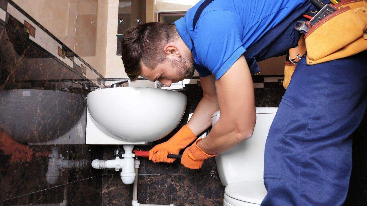 A plumber in blue overalls fixing a toilet.