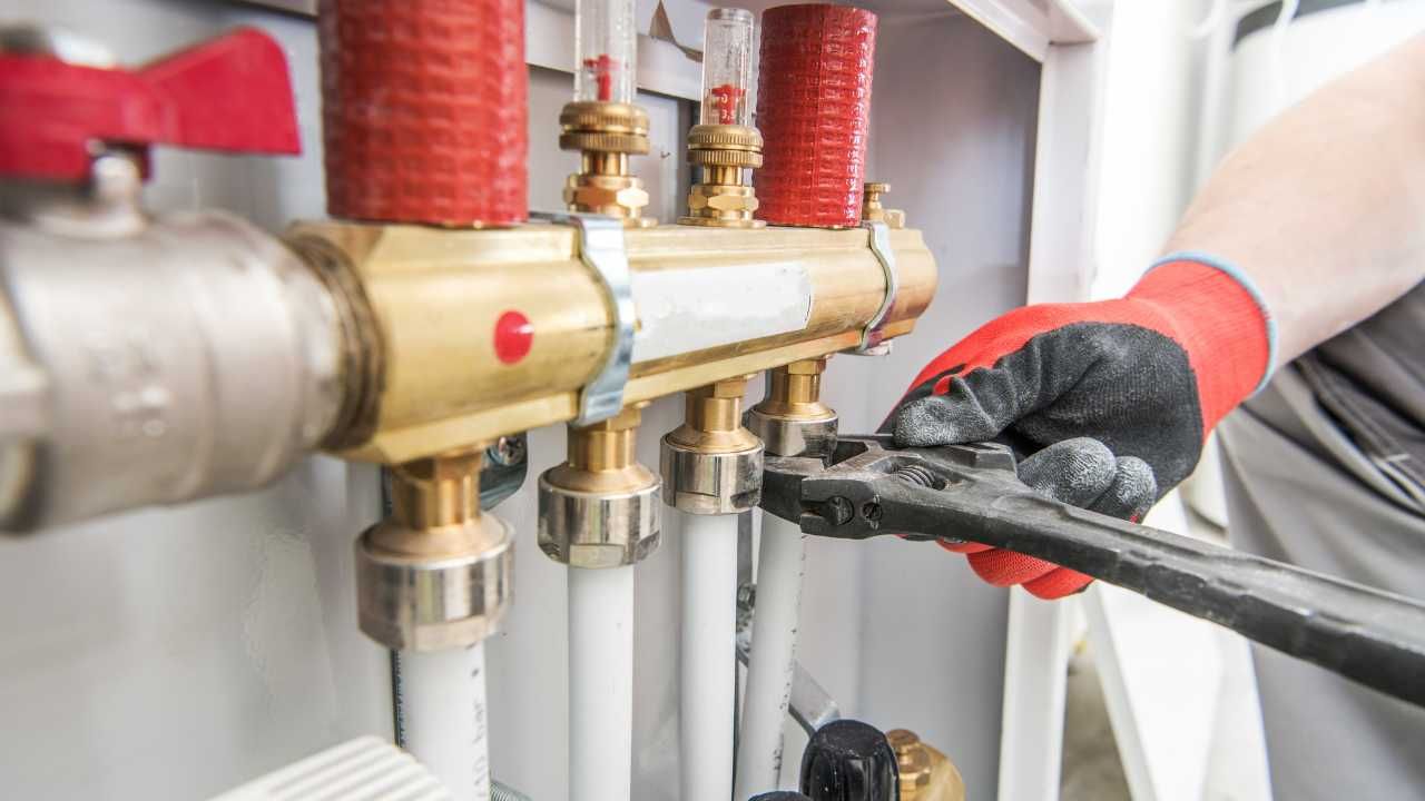 A person with a red glove is holding a wrench, fixing a pipe.