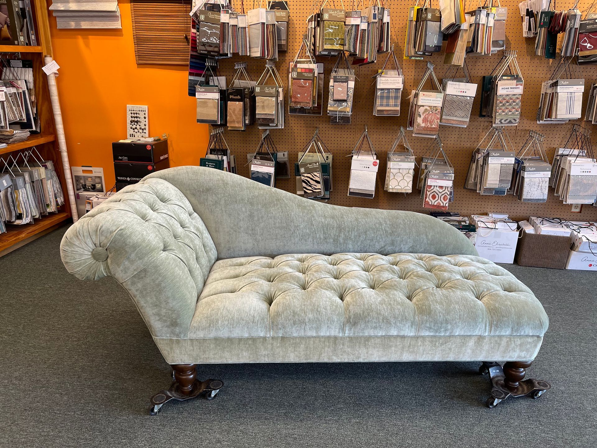 A chaise lounge is sitting in a room in front of a wall of fabric samples.