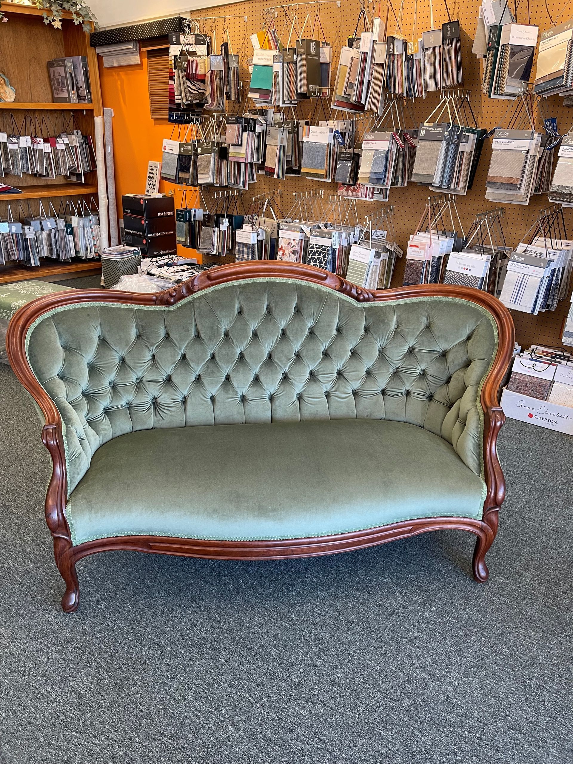 A green couch is sitting in a room in front of a wall of fabric samples.
