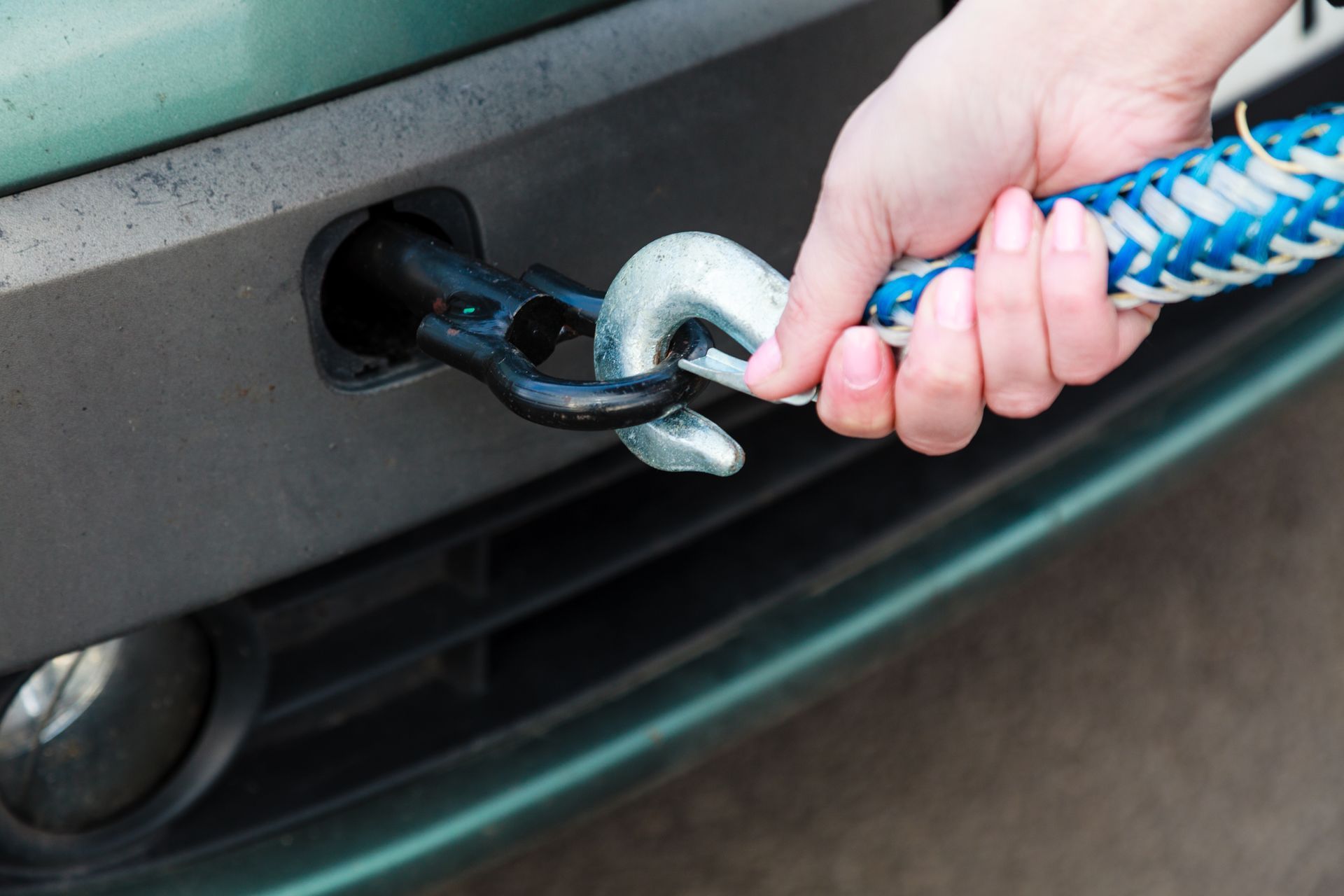 A hand attaching a tow rope hook to a car's bumper.