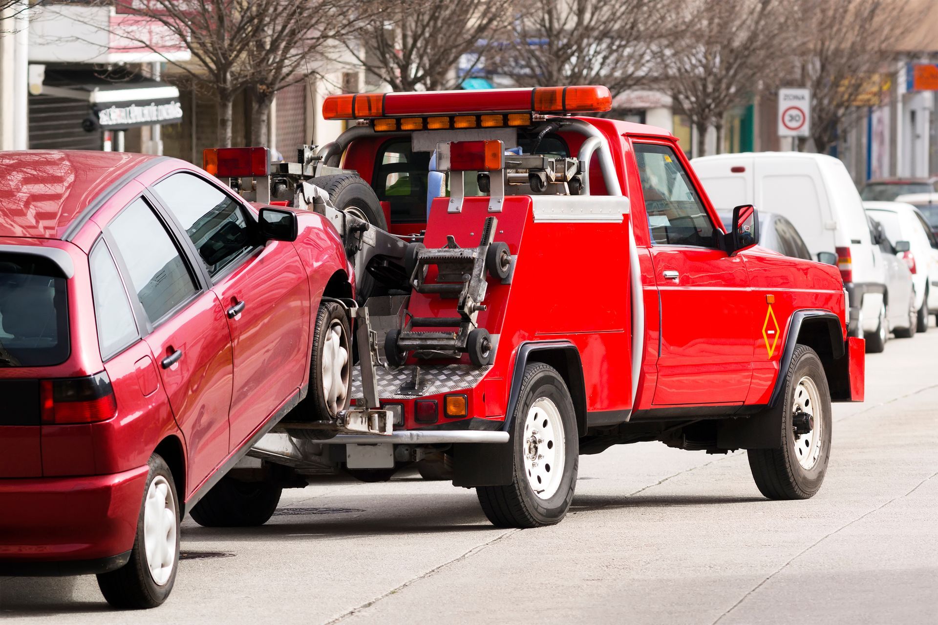 Red tow truck towing a red car on a city street.