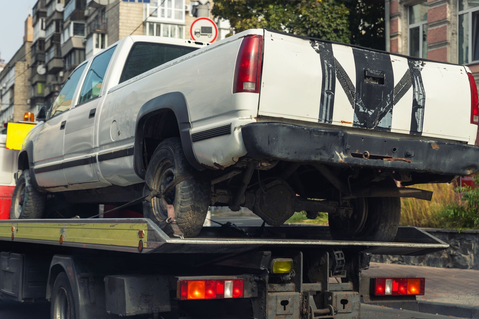 White pickup truck on a tow truck, rear view, in front of a building; daytime.