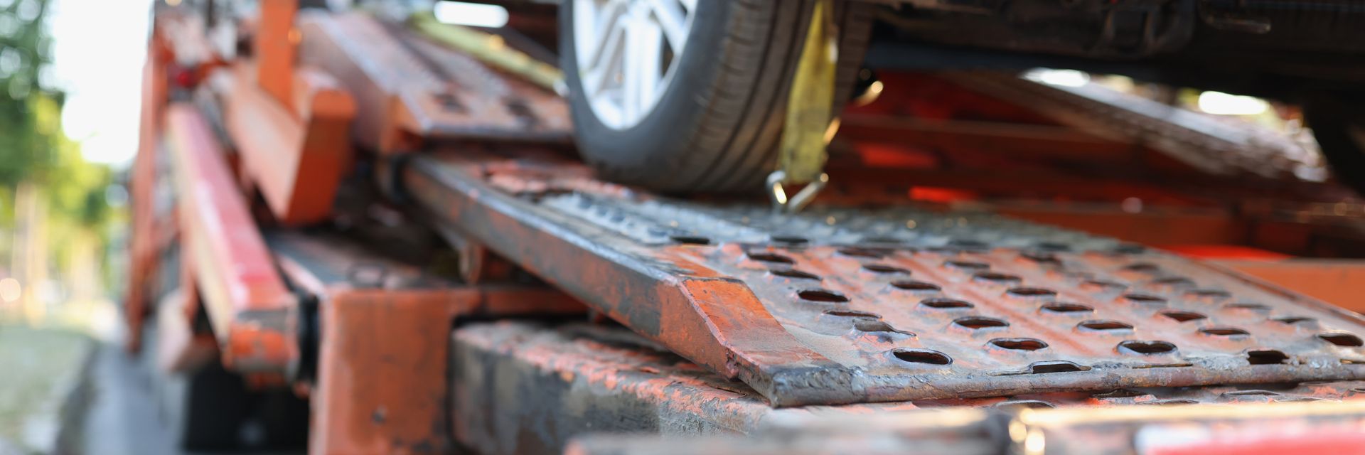 A car tire on a ramp of a tow truck. The ramp is metal and orange.