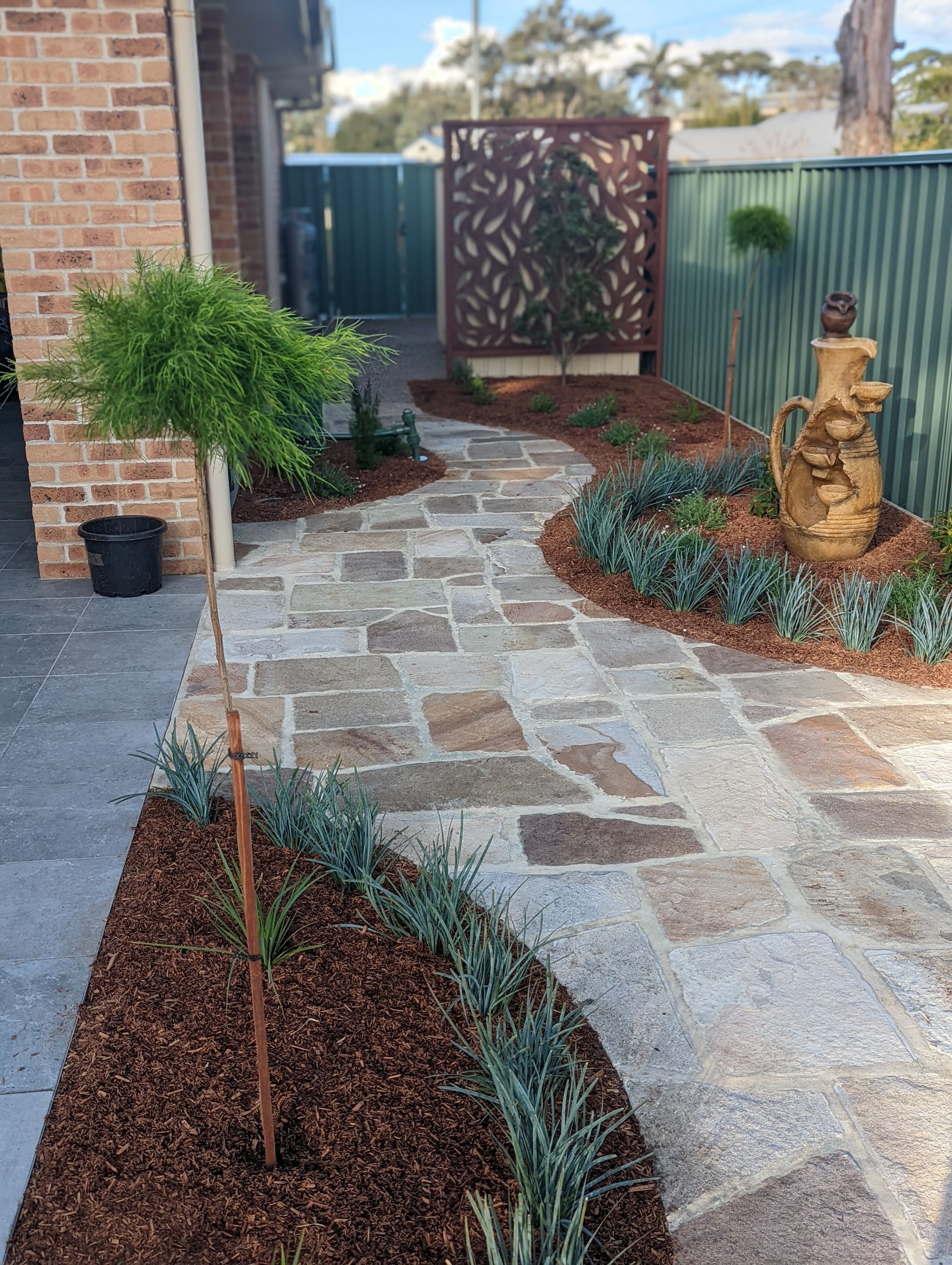 A stone walkway leading to a house with a fountain in the middle of it.