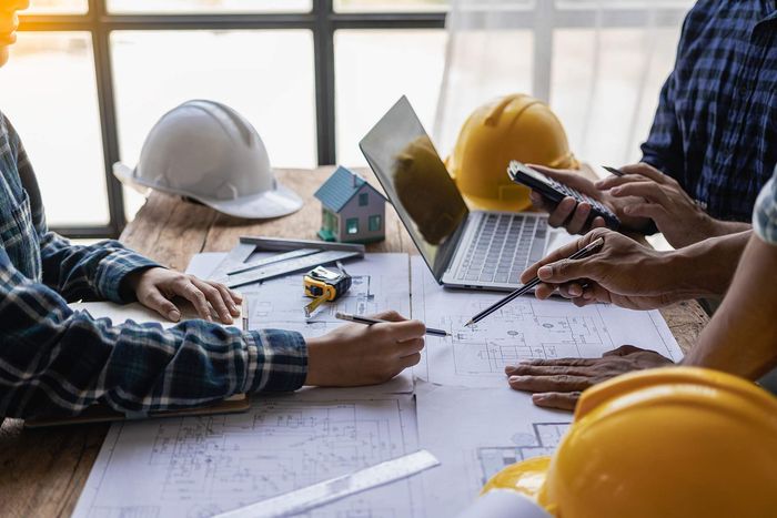 A group of construction workers are sitting at a table with hard hats and a laptop.