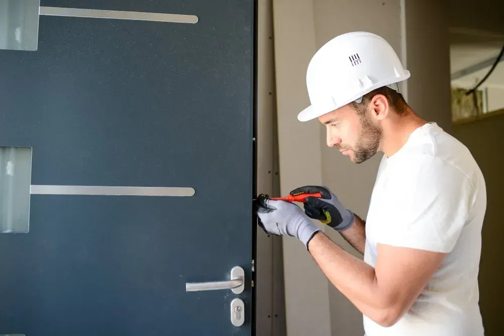 A man wearing a hard hat and gloves is working on a door.