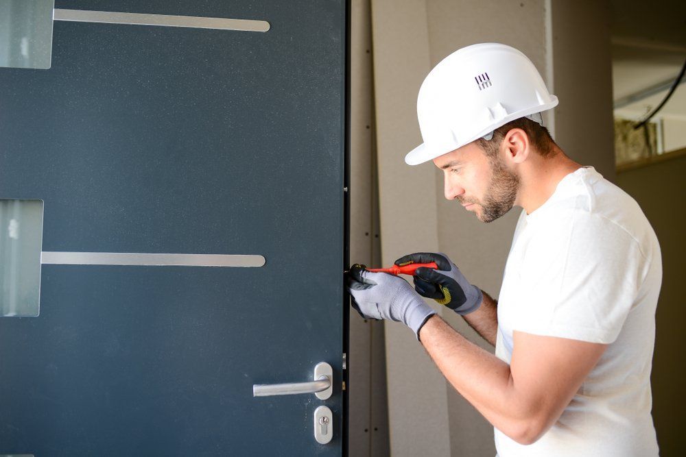 A man wearing a hard hat and gloves is working on a door.