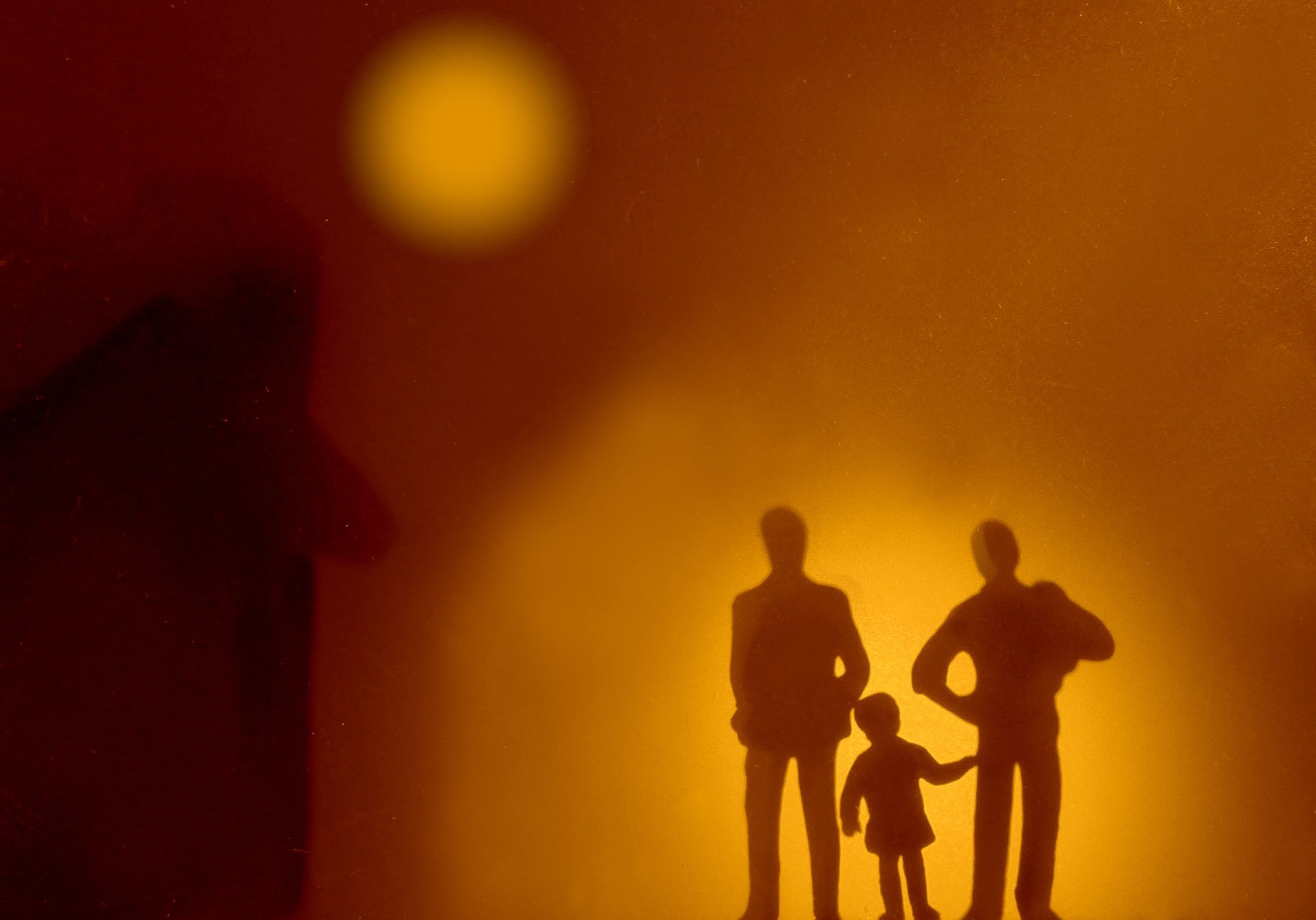 Silhouettes of three figures, two adults and one child, with a bright light in the background.