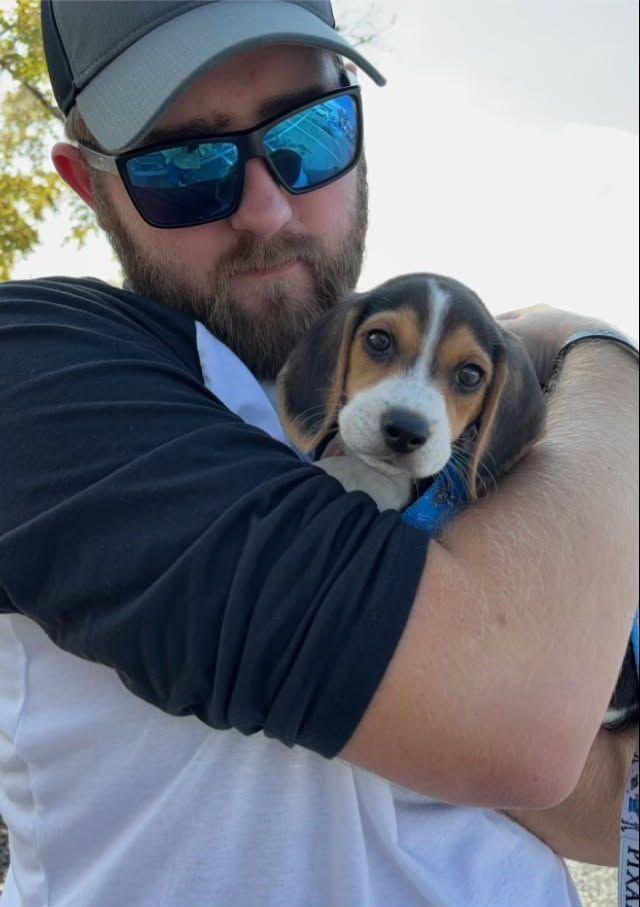 A man is holding a beagle puppy in his arms.