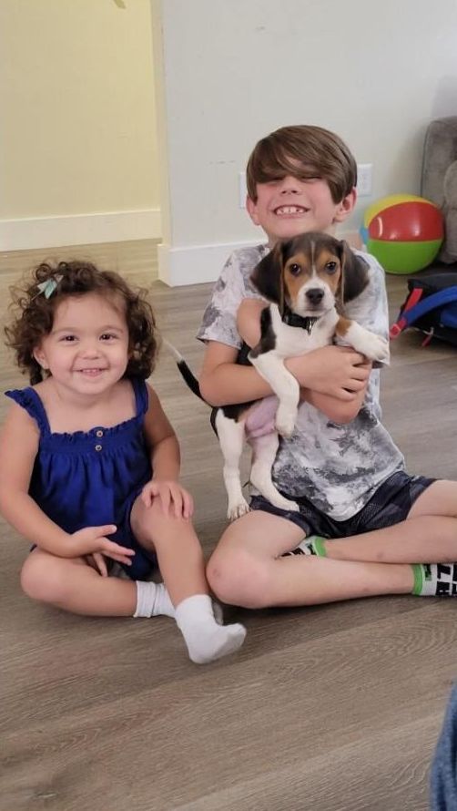 A boy and a girl are sitting on the floor holding a puppy.