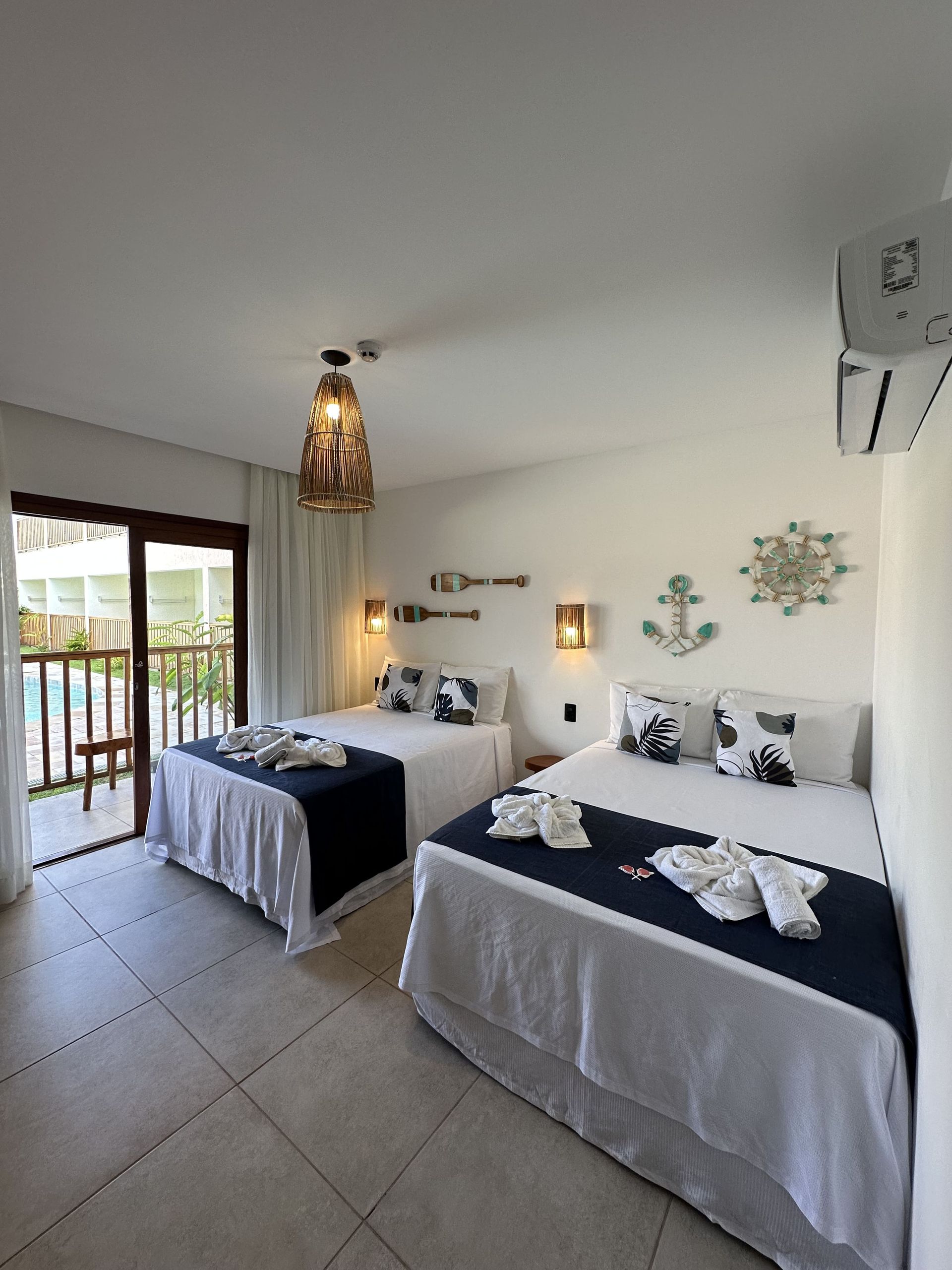 Quarto com duas camas, decoração náutica: detalhes em azul, roupa de cama branca, vista para a varanda.