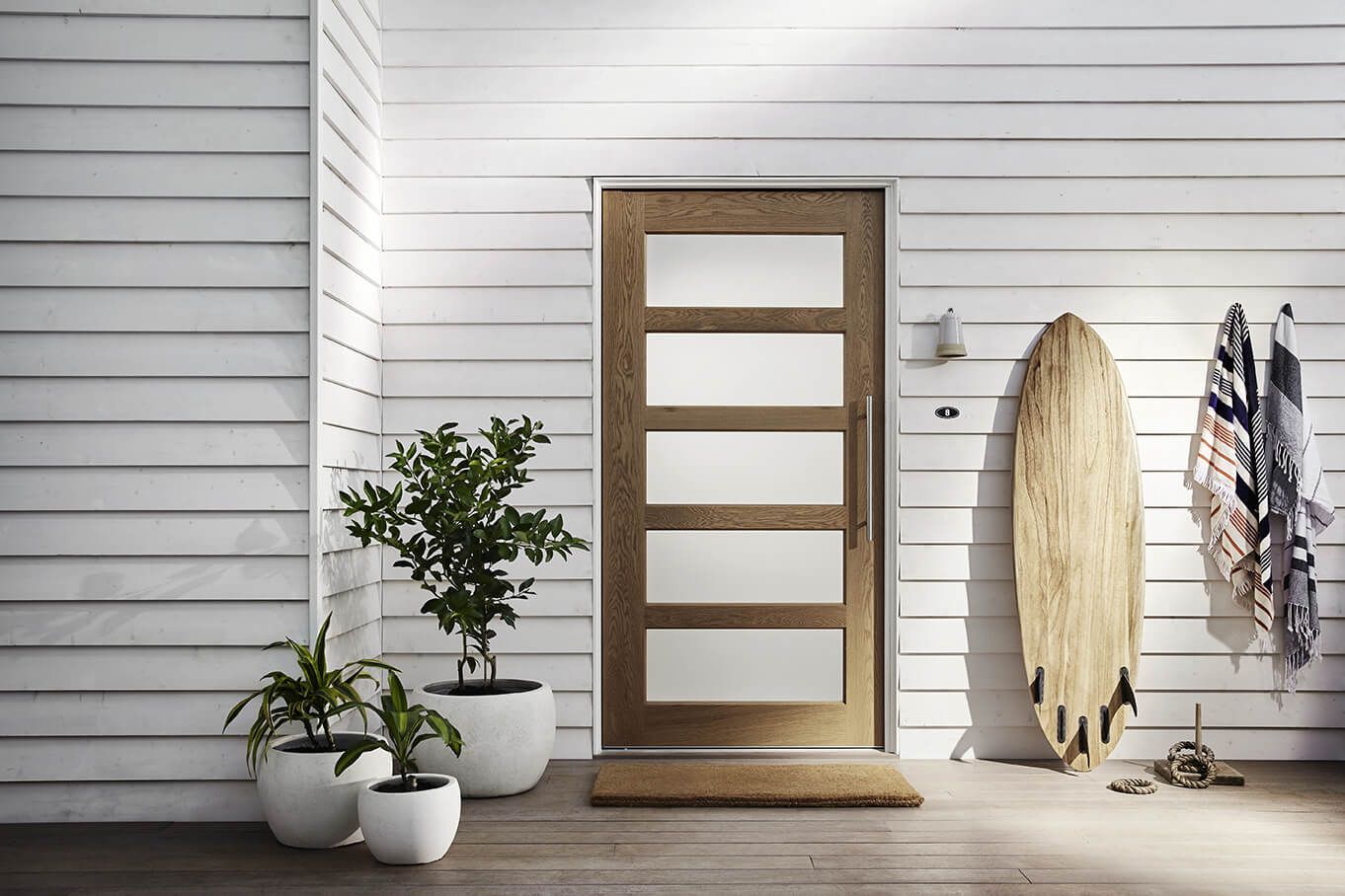 A White House with A Wooden Door and A Surfboard in Front of It — Bootle Timber QLD Pty Ltd in Garbutt, QLD